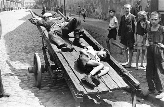 Two destitute boys sleep on a cart parked on a street in the Warsaw ghetto